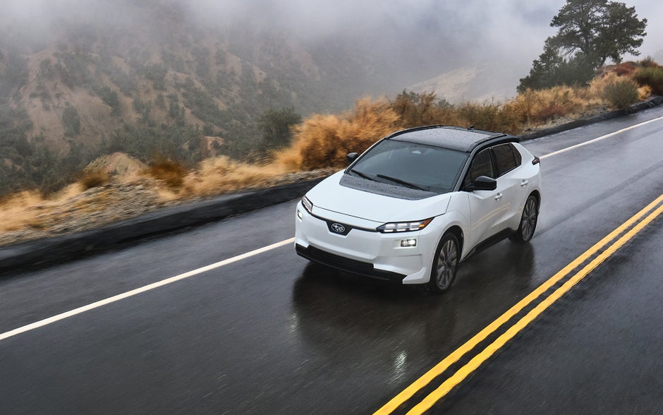 A Solterra AWD electric SUV drives on a narrow mountain road in the rain.